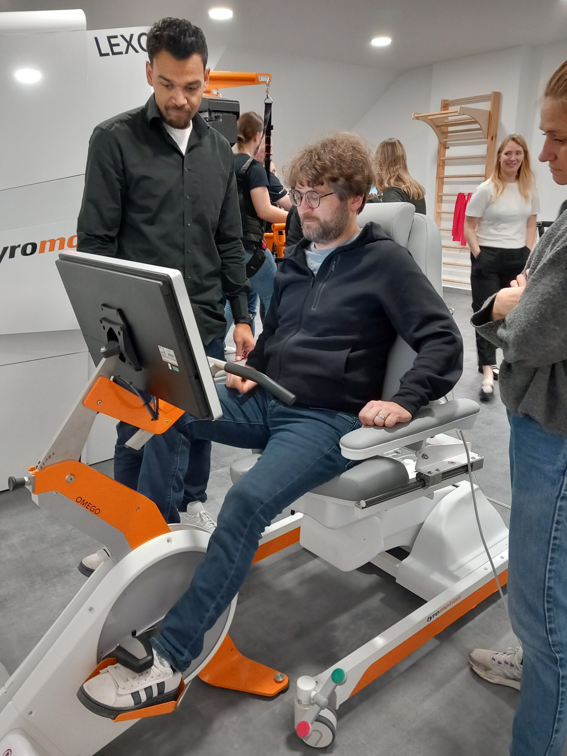 Recap: “Robotics in Rehab” Workshop – Insights, Exchange & Innovation: One person trying gait trainer Omego Plus, 2 others standing beside