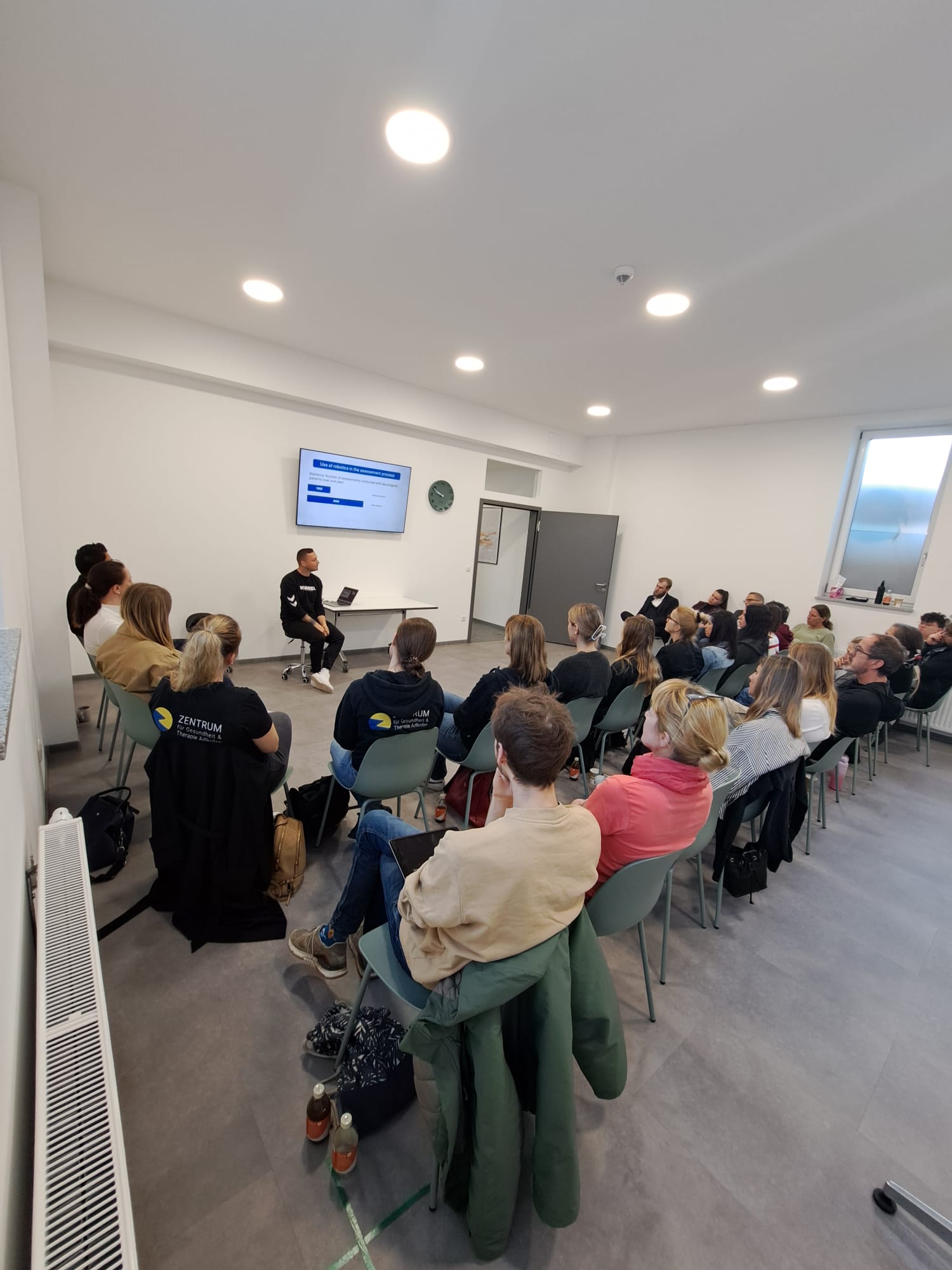Recap: “Robotics in Rehab” Workshop – Insights, Exchange & Innovation: All attendees are sitting in a therapy room, listening interested to a therapist in the front