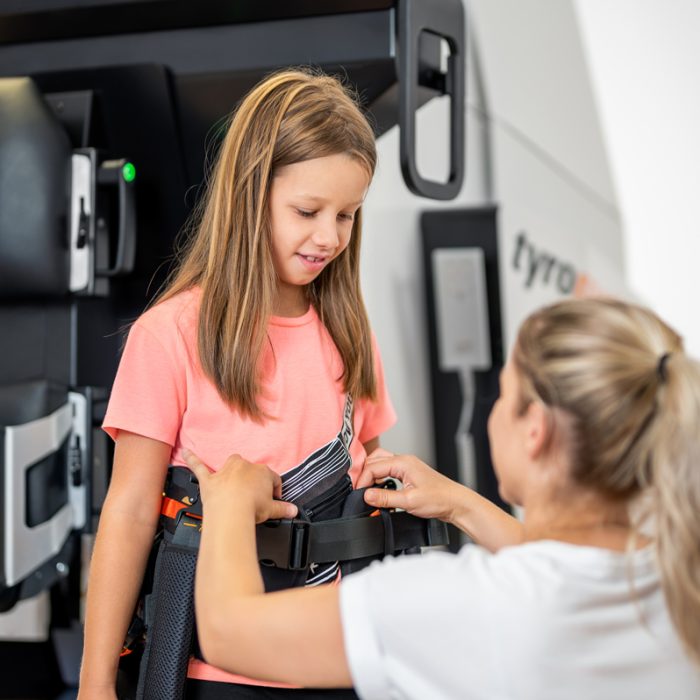 Therapist securing a harness on a young girl for the Lexo gait trainer.