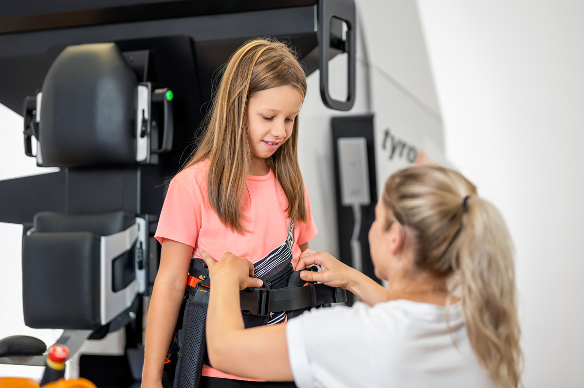 Therapist securing a harness on a young girl for the Lexo gait trainer.