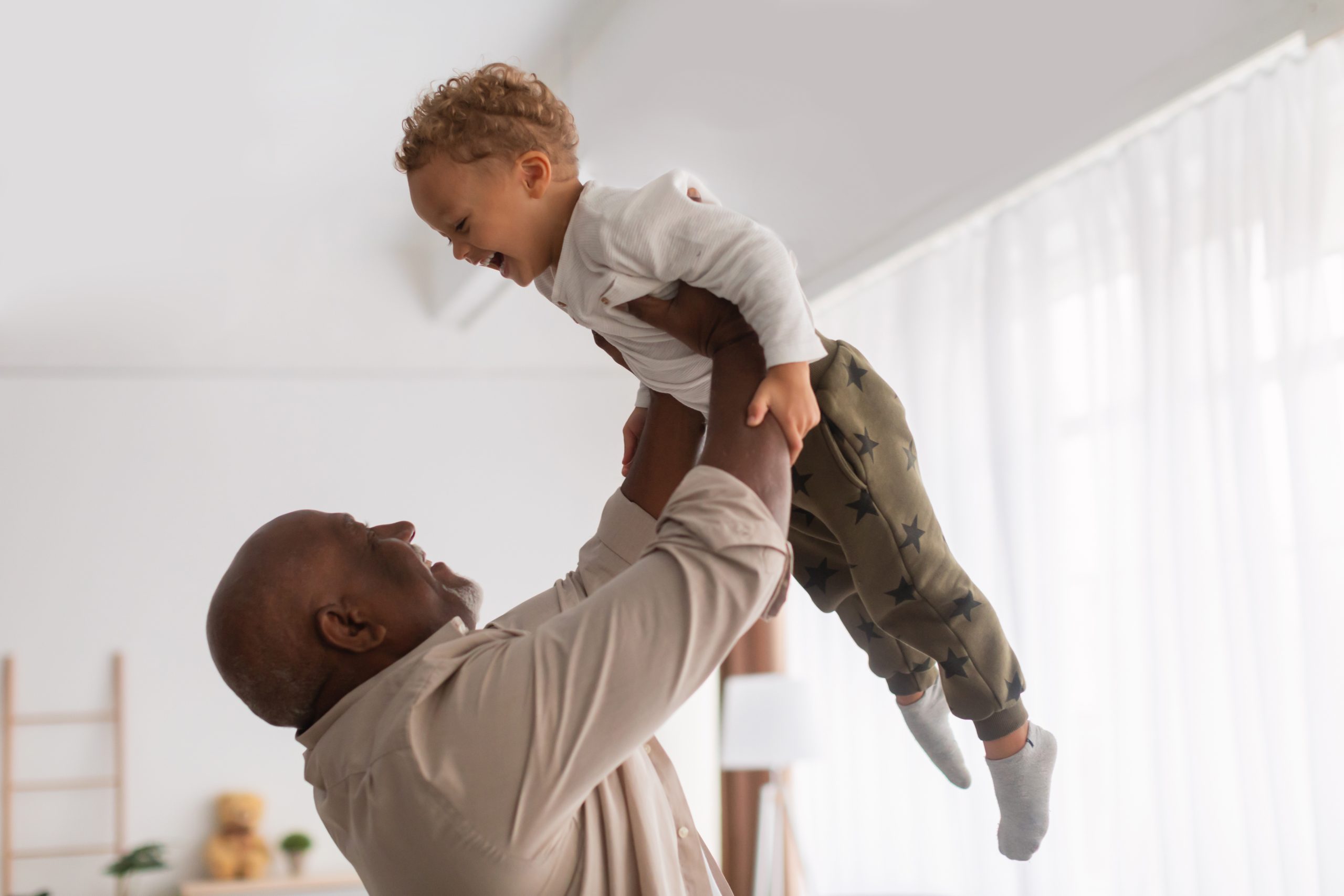 Father lifting his child in a bright room, both smiling and joyful.