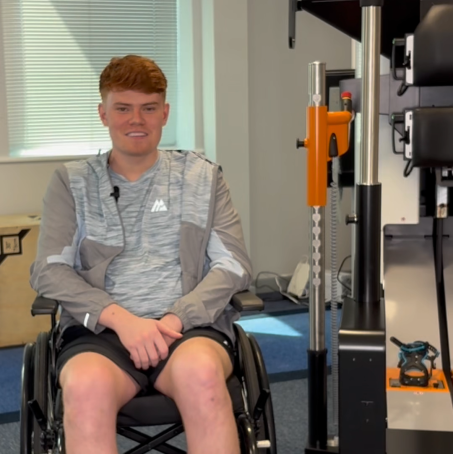 Sam Kitchen sitting in his wheelchair next to gait trainer Lexo