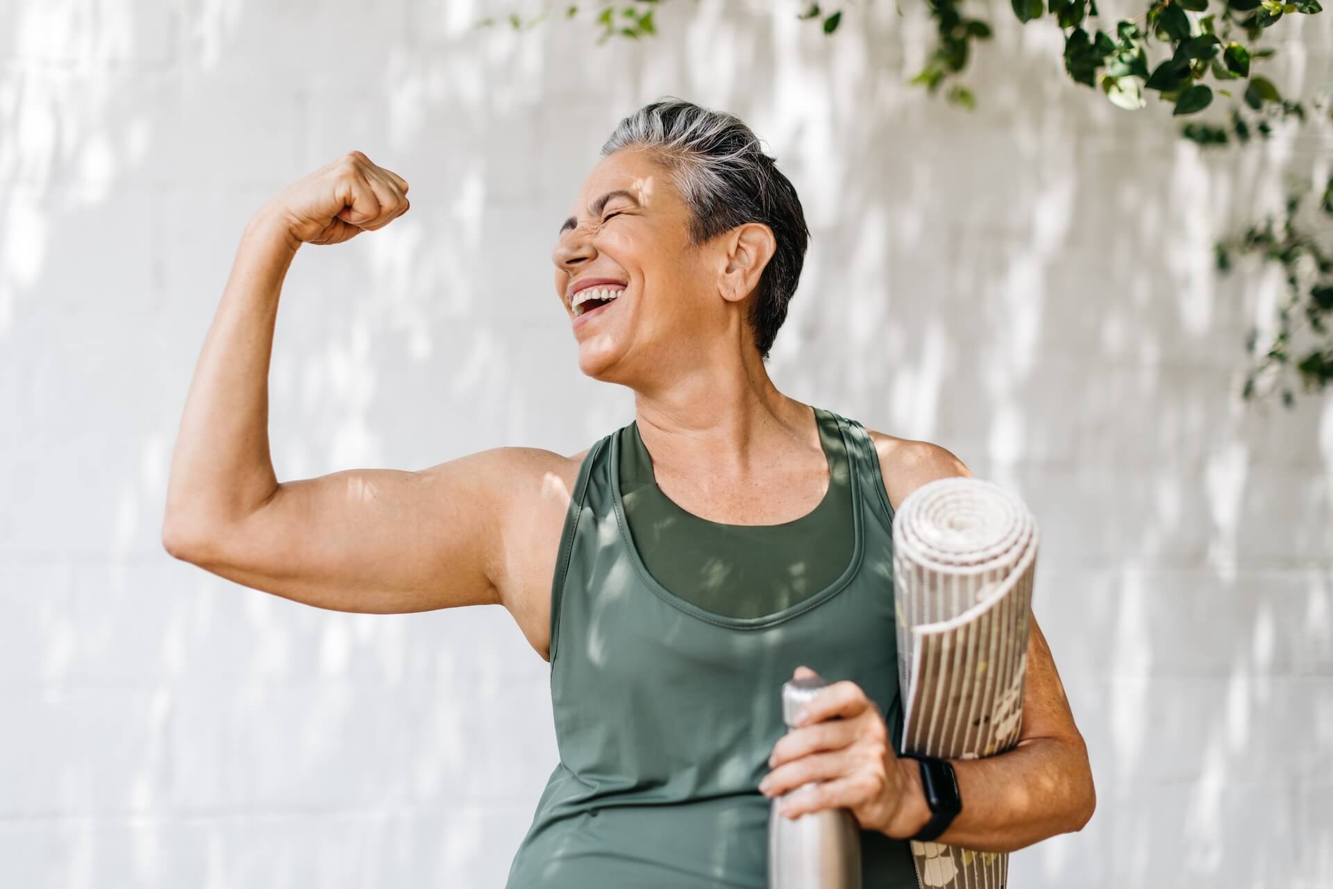 Motivated woman in athletic wear carrying a yoga mat and water bottle after therapy or exercise.