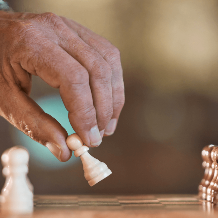 Hand reaching for a chess piece on a chessboard surrounded by other pieces.