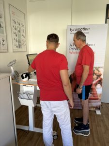 Therapist and Patient, both in red t-shirts during therapy session with Tymo. Josef is in MS Rehabilitation at Radkersburger Hof.