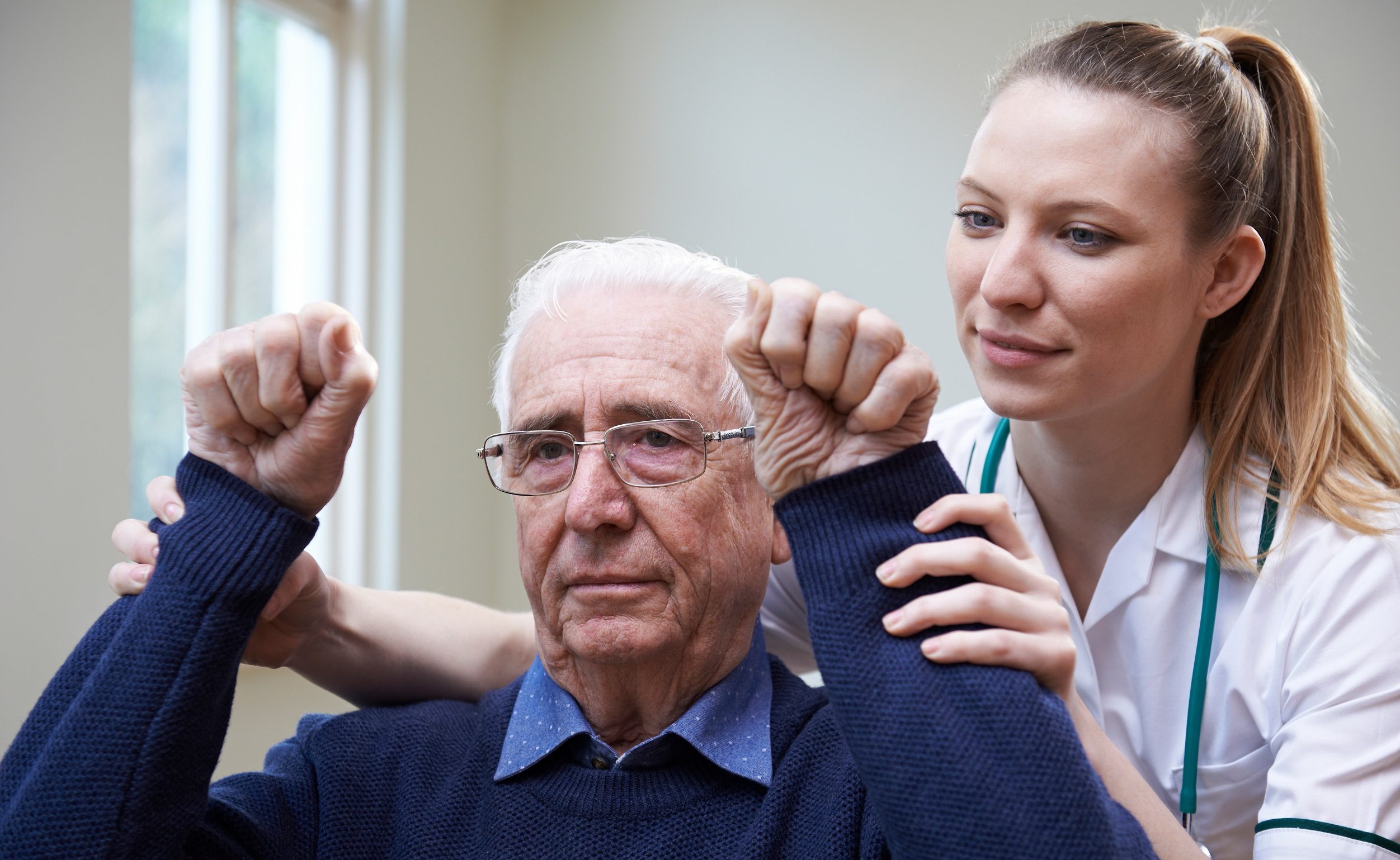 Female nurse is assisting a older man, stroke victim by raising his hands