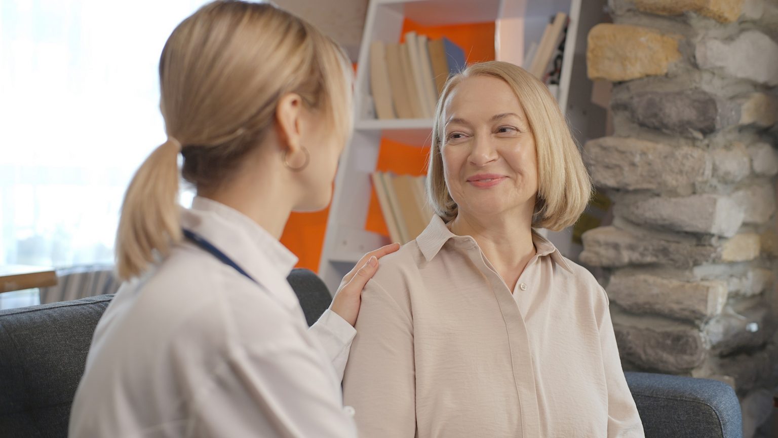 Young woman which seems to be a therapist or doctor is talking to a sick old woman