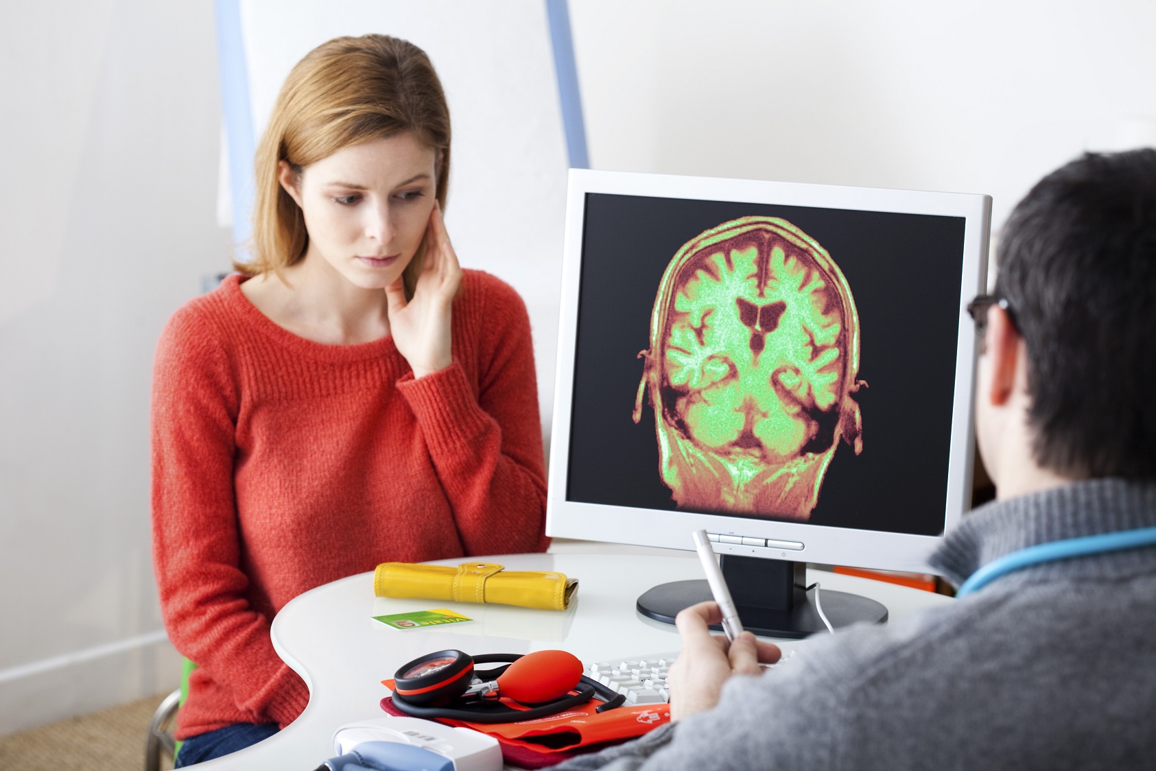 Female patient talking with a male doctor. On a computer screen is a picture of a brain visible.