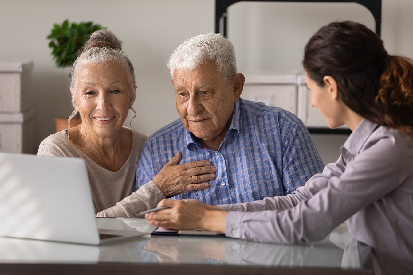 An older couple sitting at the doctor and looking into a screen with therapy data while a female doctor speaks with them