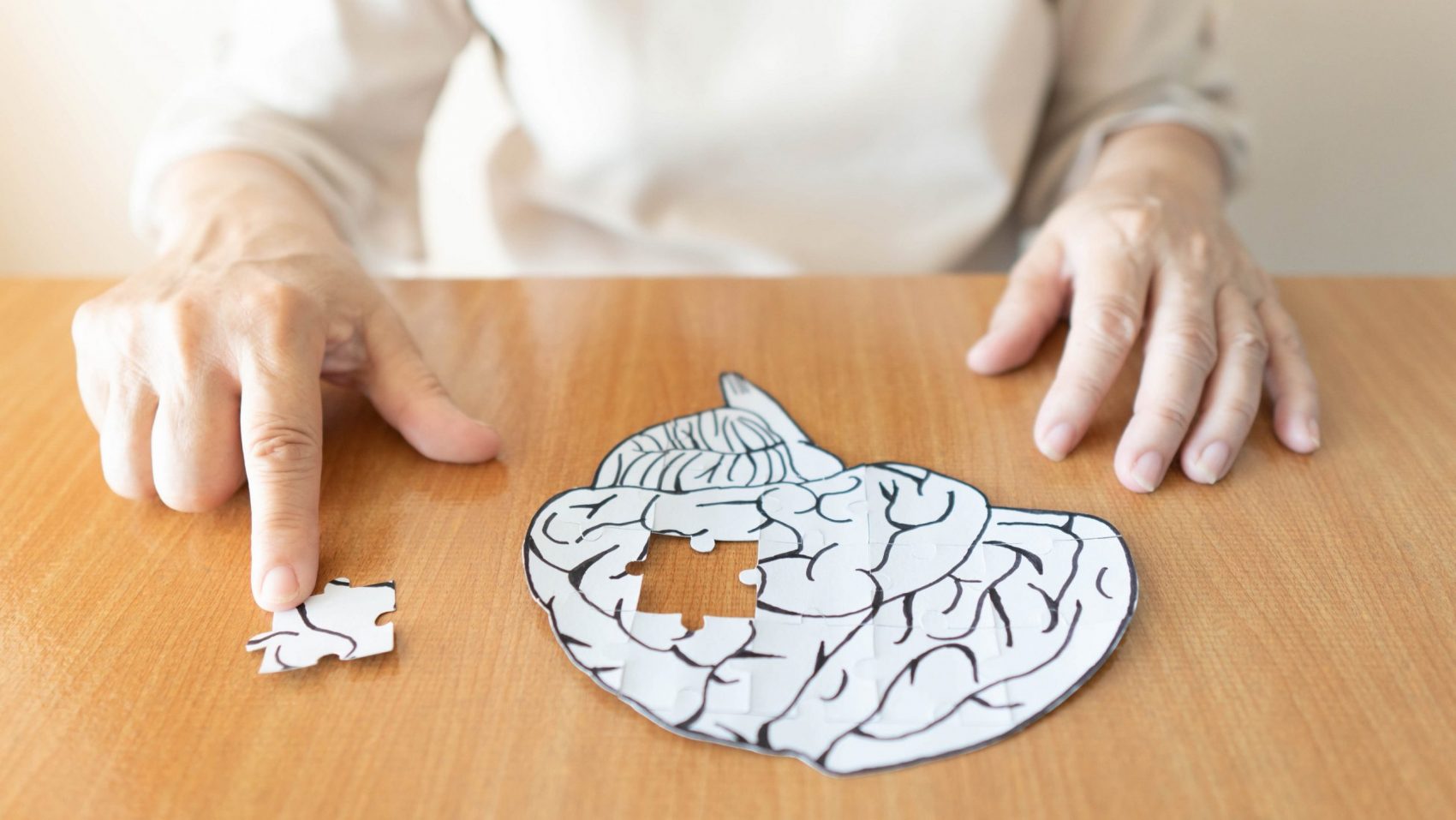Hands of an elderly woman putting missing puzzle from a brain pieces together