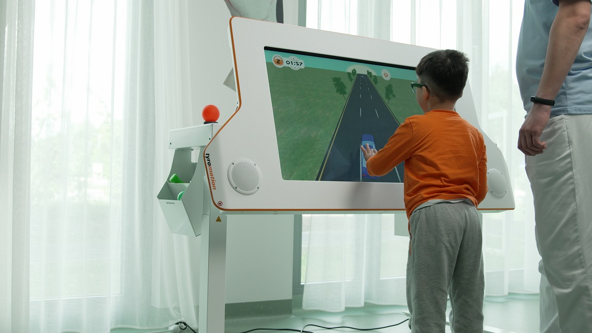 A male child in a therapy room using the interactive rehabilitation device Myro and a therapist standing by his side
