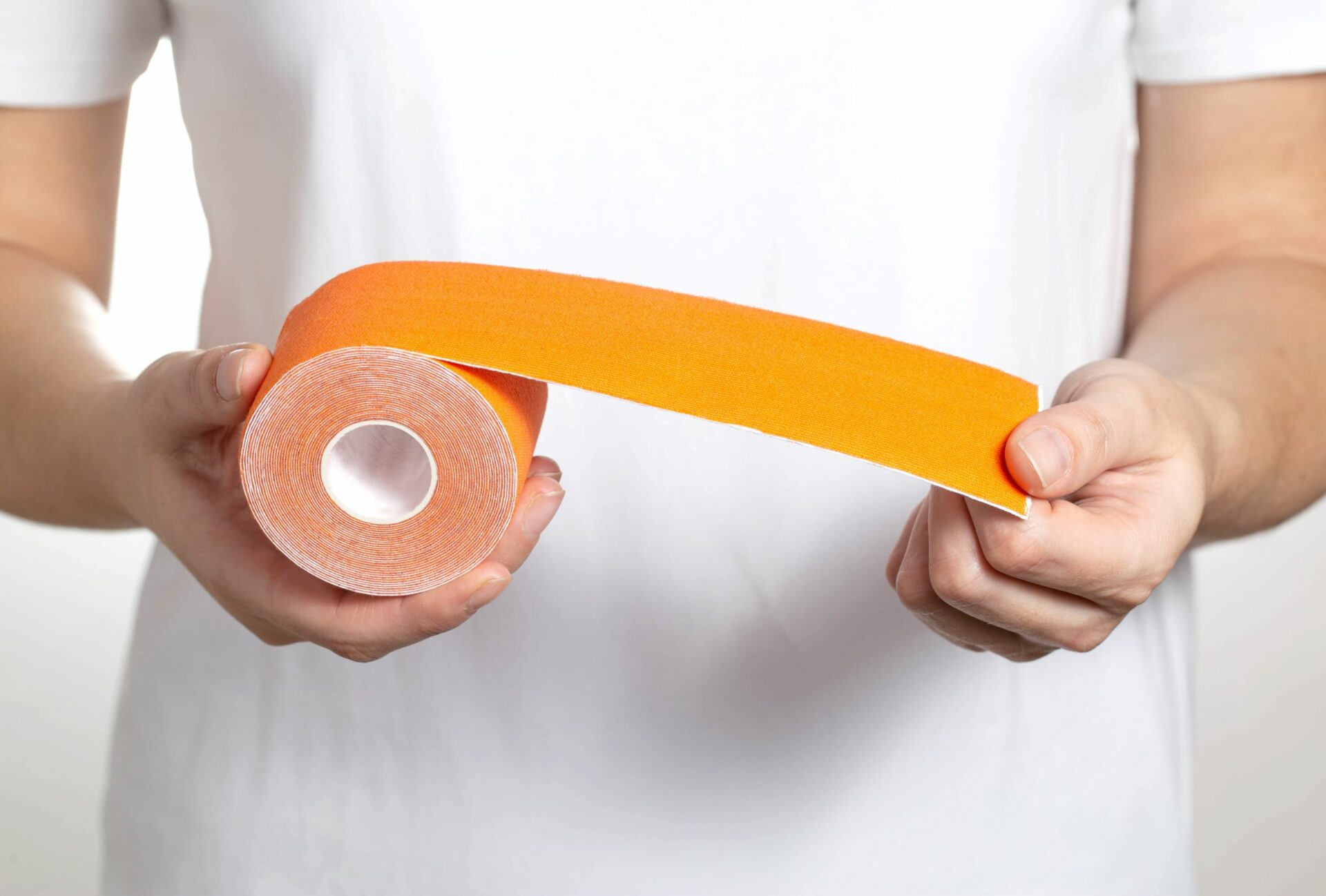 Therapist holds orange kinesiology tape in hands